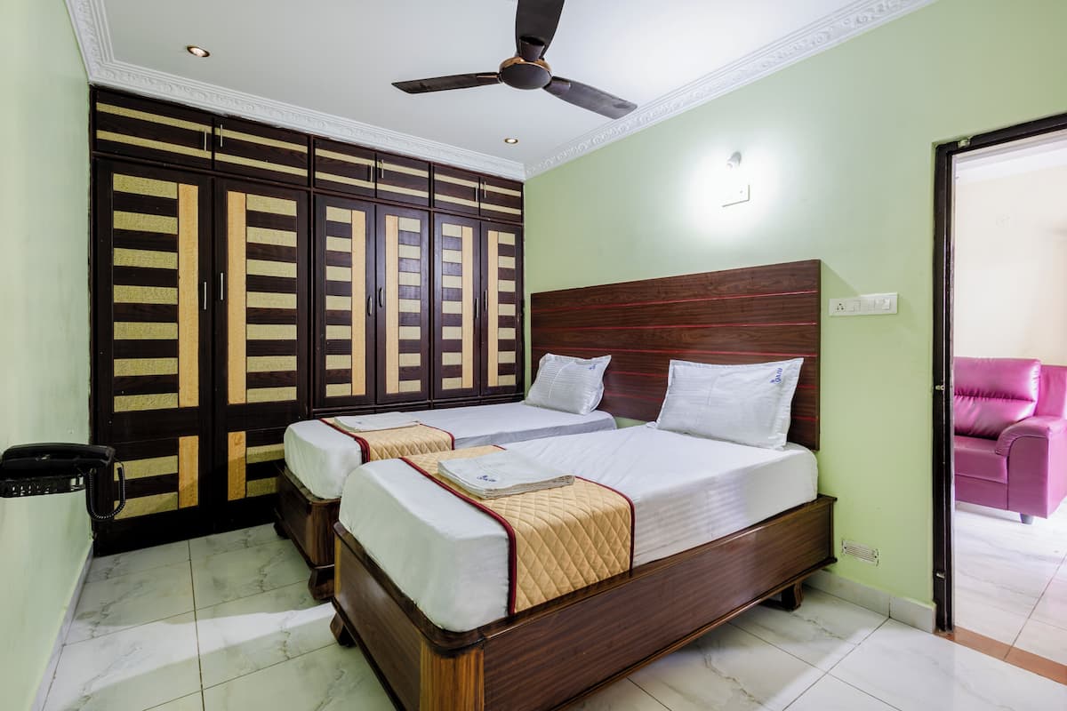 A hotel room with a large wardrobe, two beds, a ceiling fan, and a pink chair.