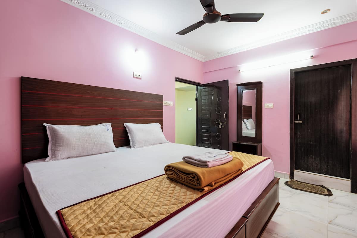 A hotel room with a bed, a ceiling fan, a door, and a mirror.