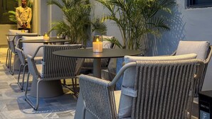 A modern outdoor seating area with round tables and wicker chairs, surrounded by potted plants.