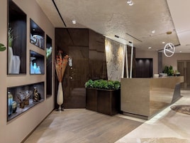 Una moderna area reception con una scrivania a forma di arco, opere d'arte a parete e un vaso decorativo con piante essiccate.