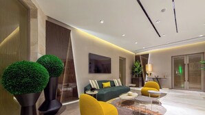 A modern living room with a sofa, yellow pouf, and two spherical green plants.