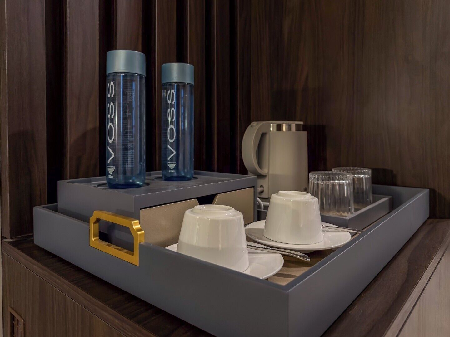 Una bandeja con dos botellas azules, una taza blanca y tazas blancas.
