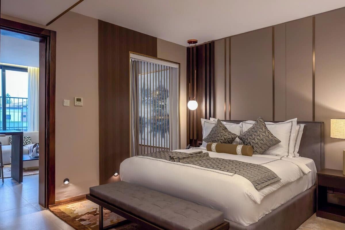 A modern bedroom with a large bed, bedside tables, a bench, and a view of the outdoors.