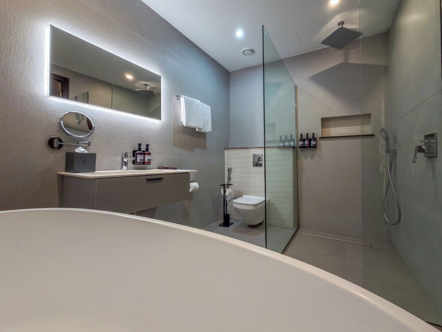 Un baño moderno con bañera, inodoro, ducha y tocador con espejo y artículos de aseo.