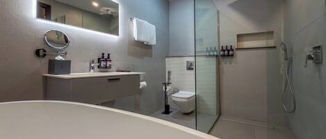 Un baño moderno con bañera, inodoro, ducha y tocador con espejo y artículos de aseo.