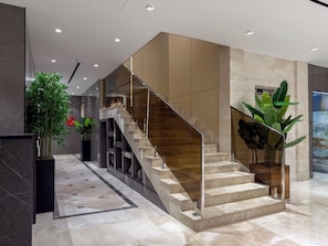 A modern interior with a marble staircase, glass railings, and potted plants.