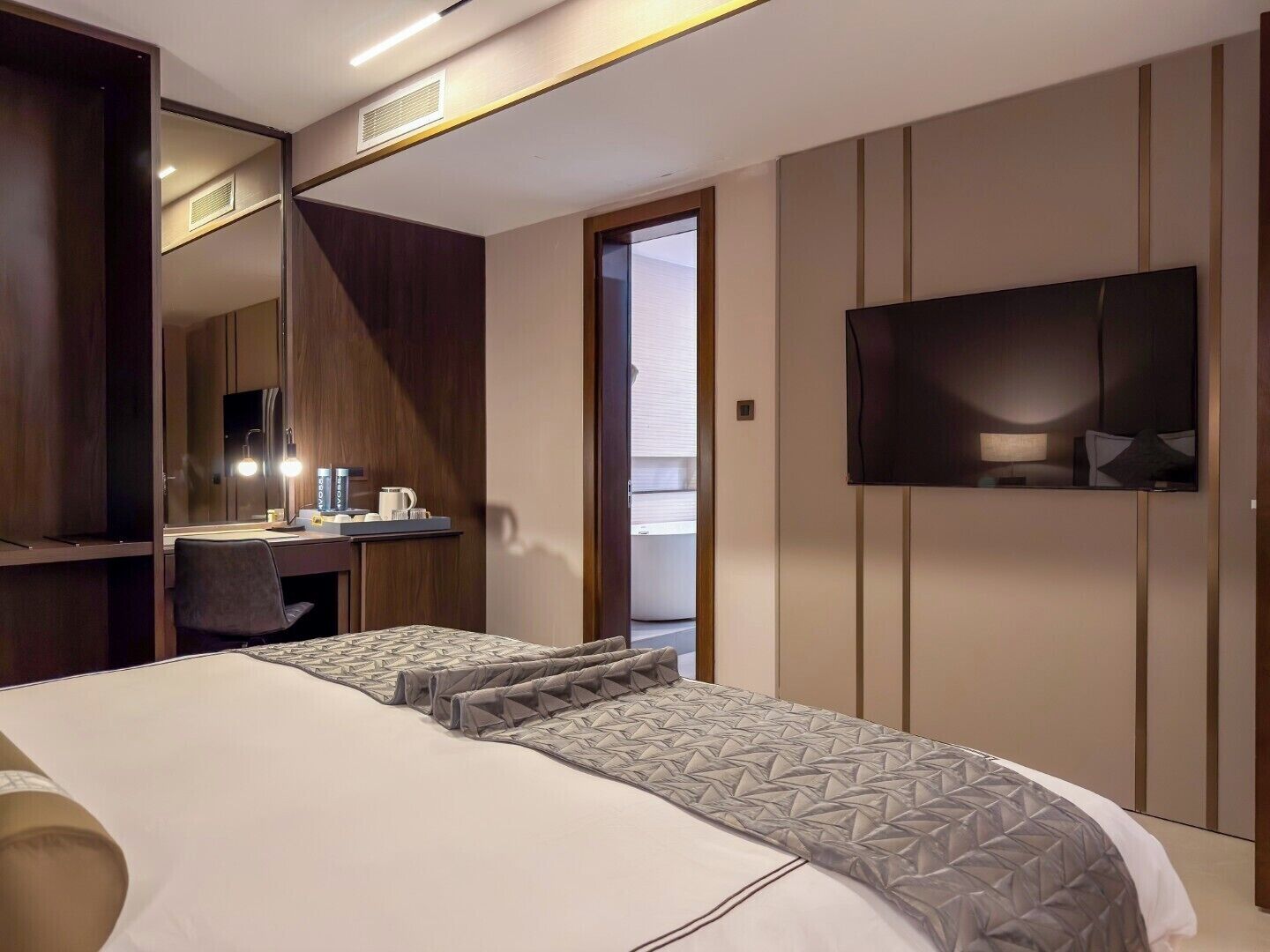 Een moderne hotelkamer met een groot bed, een bureau met spiegel, een aan de muur bevestigde televisie en een balkon.