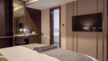 Een moderne hotelkamer met een groot bed, een bureau met spiegel, een aan de muur bevestigde televisie en een balkon.