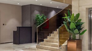 A modern interior with a marble staircase, a reception desk, and potted plants.