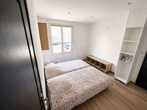 A bedroom with two beds, a window, a built-in bench, and a wardrobe. - Le cocon Portelois (Le Portel)