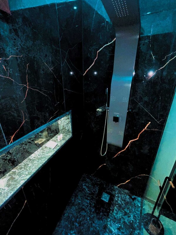 A bathroom with a glass enclosure, a handheld showerhead, and a marble floor.