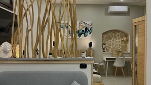 A modern living room with a grey sofa, a wooden decorative wall, a stone fireplace, and a dining area with a white table and chairs. - House with hot tub ( BRAMA WELLNESS EXPERIENCE) (Brindisi)