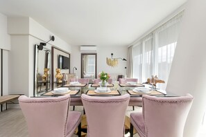 Een eetruimte met een glazen tafel, roze gestoffeerde stoelen en een vaas met bloemen.