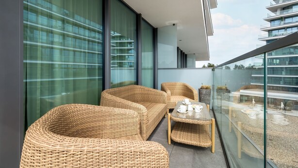 A balcony with wicker furniture, a glass table, and a view of other buildings. - Bluewave - Wave Resort & Spa (Mi ędzyzdroje)