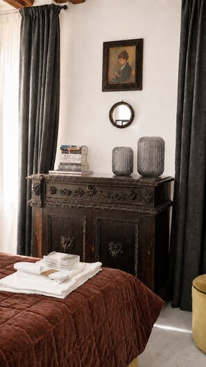 Ein Schlafzimmer mit einem braunen Bett, einer Holzkommode mit dekorativen Schnitzereien, einem Bücherstapel und einem gerahmten Bild an der Wand.