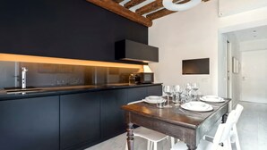 Eine moderne Küche mit dunklen Schränken, einem Holztisch gedeckt mit Tellern und Gläsern sowie einem an der Wand befestigten Fernseher.
