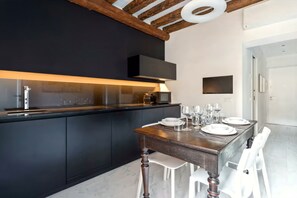 Eine moderne Küche mit dunklen Schränken, einem Holztisch gedeckt mit Tellern und Gläsern sowie einem an der Wand befestigten Fernseher.