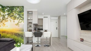 A modern kitchen with white cabinets, a dining area with two bar stools, and a TV mounted on the wall. - Nubo - Wave Resort & Spa (Międzyzdroje)