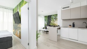 A modern kitchen with white cabinetry, a dining area with a sofa and table, and a bedroom with a bed and curtains. - Nubo - Wave Resort & Spa (Międzyzdroje)