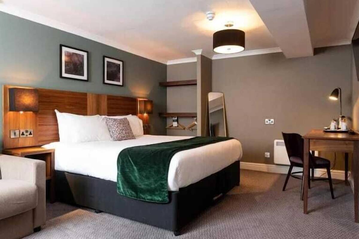 A hotel room with a bed, bedside tables, a desk, a chair, and a mirror.