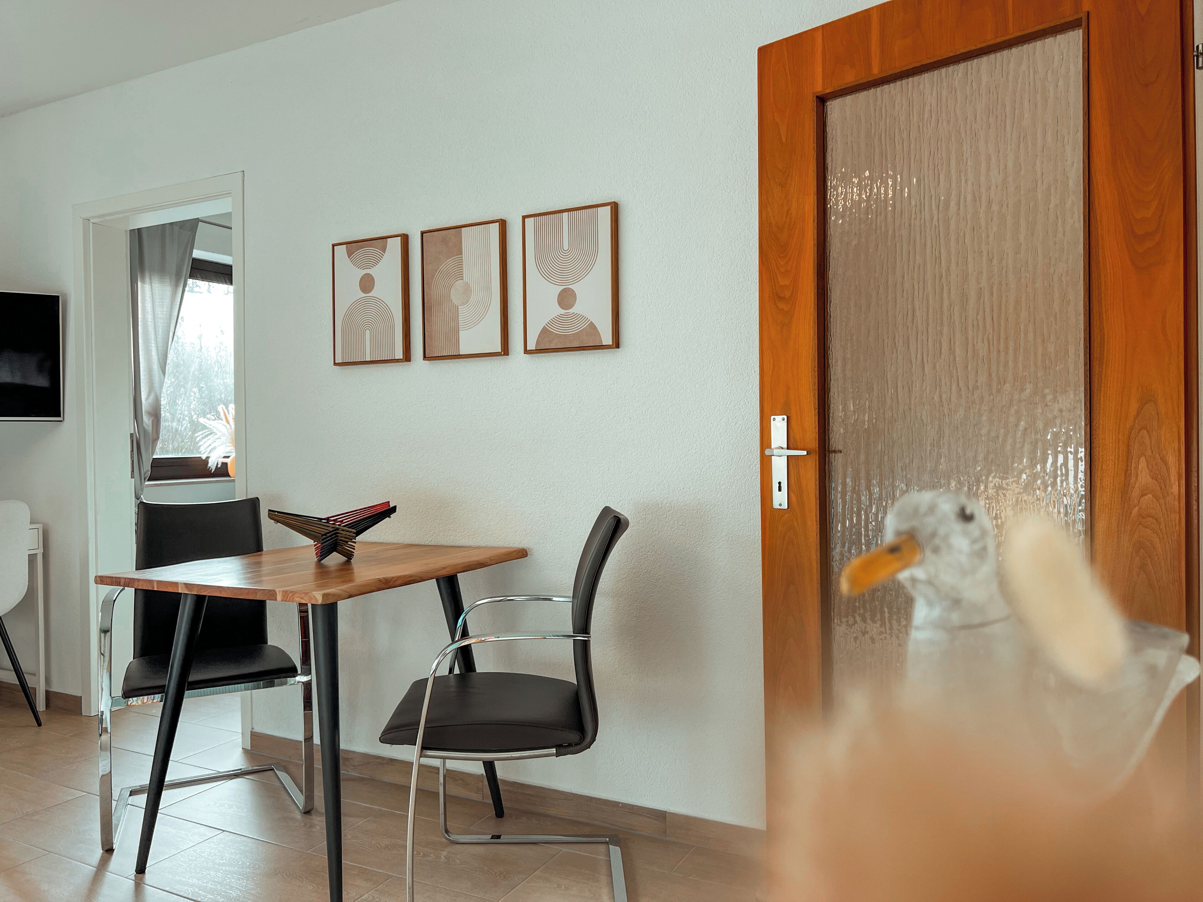 Une pièce avec une porte en bois, une table à manger entourée de chaises et trois œuvres d’art encadrées accrochées au mur.