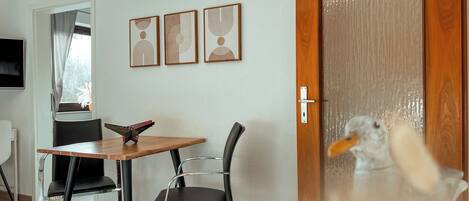 Une pièce avec une porte en bois, une table à manger entourée de chaises et trois œuvres d’art encadrées accrochées au mur.