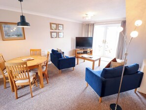 Ein Wohnzimmer mit Esstisch, blauen Sofas, Fernseher und Stehlampe.
