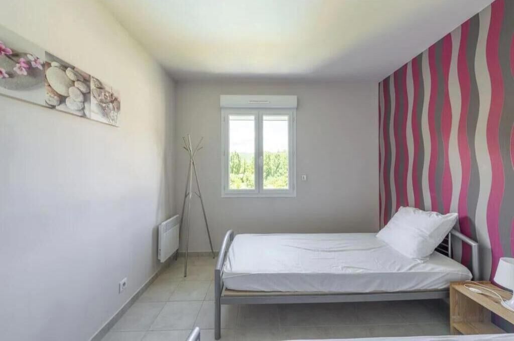 A bedroom with a bed, a radiator, a window, and a wall with a striped pattern.