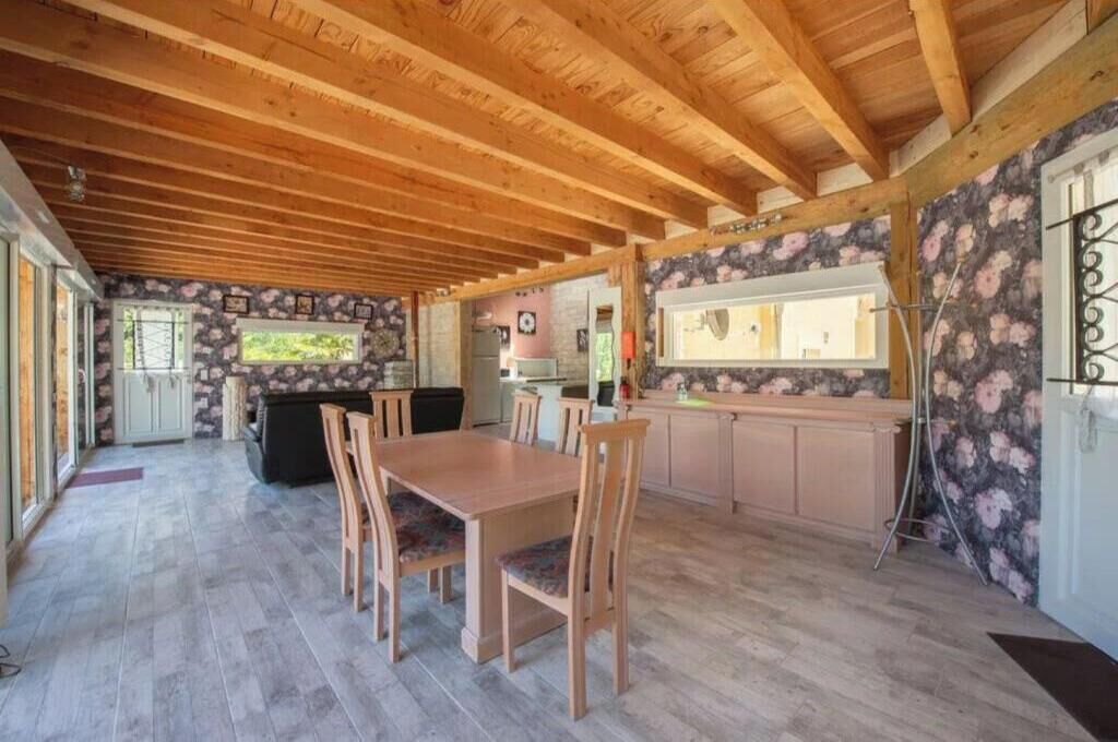 A spacious kitchen with wooden beams, a dining area with chairs, and a stone wall with floral wallpaper.