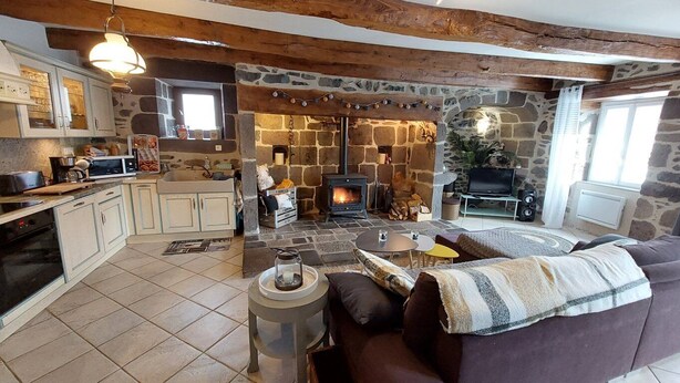 A cozy living room with a stone fireplace, a sofa, and a kitchen area with a microwave. - Charming 6-person house with large terrace - near Salers and Puy Mary (Anglards-de-Salers)