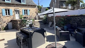 A stone building with a patio area featuring outdoor furniture and a table set for dining. - Charming 6-person house with large terrace - near Salers and Puy Mary (Anglards-de-Salers)
