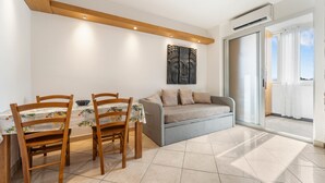 A dining area with a table and chairs, a sofa, a wall-mounted artwork, and a sliding glass door leading to an outdoor space. - Home Karalis Apartment (Su Planu)