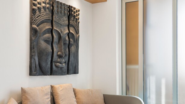 A modern living room with a sofa, cushions, and a large stone sculpture on the wall. - Home Karalis Apartment (Su Planu)