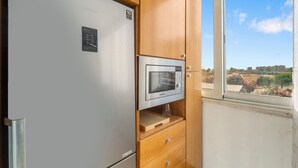 A compact kitchen with a built-in microwave, a refrigerator, and a window with a view of the cityscape. - Home Karalis Apartment (Su Planu)