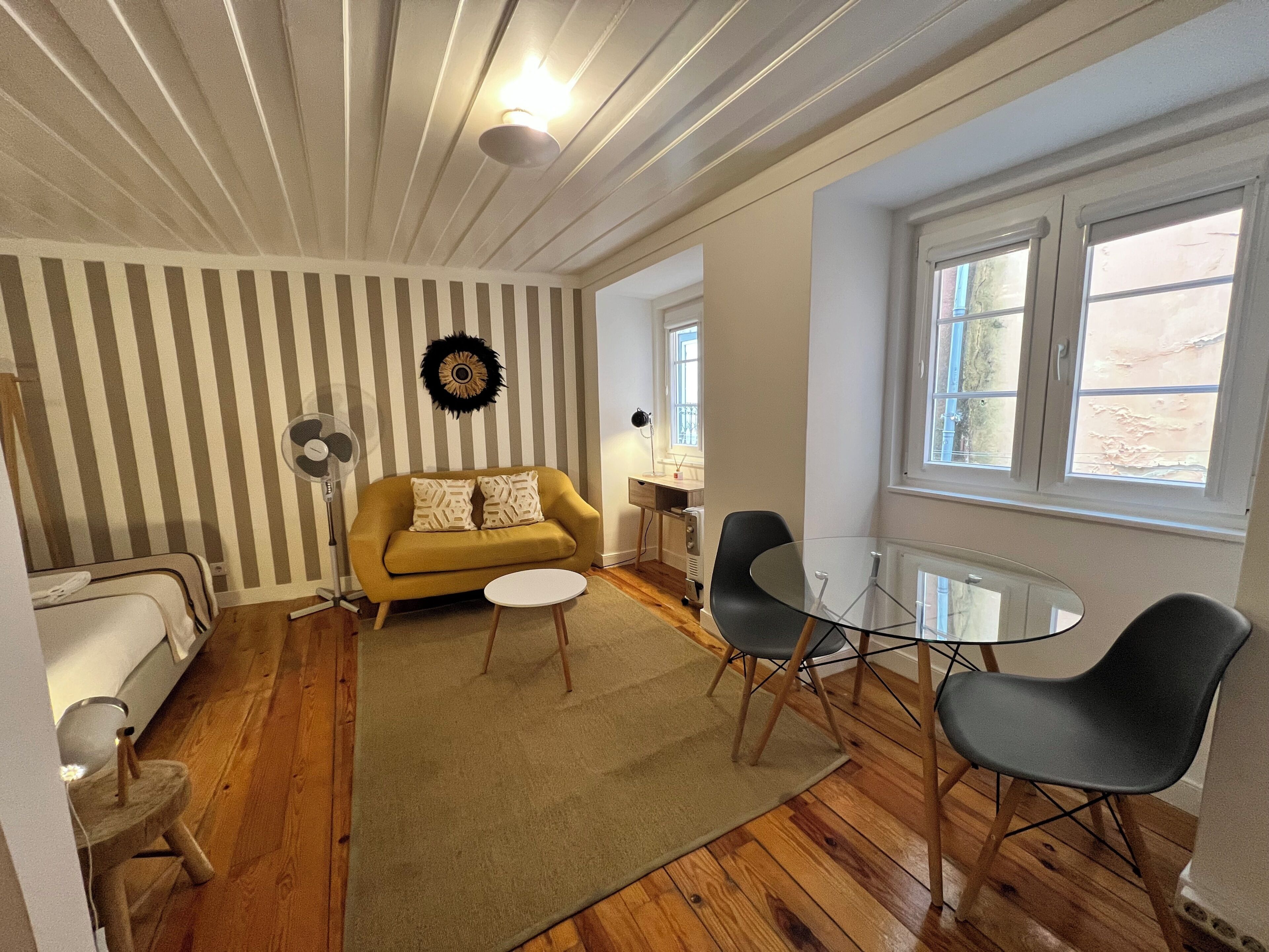 Une pièce avec un mur à rayures, un canapé, une petite table ronde, deux chaises, un lampadaire et une fenêtre.
