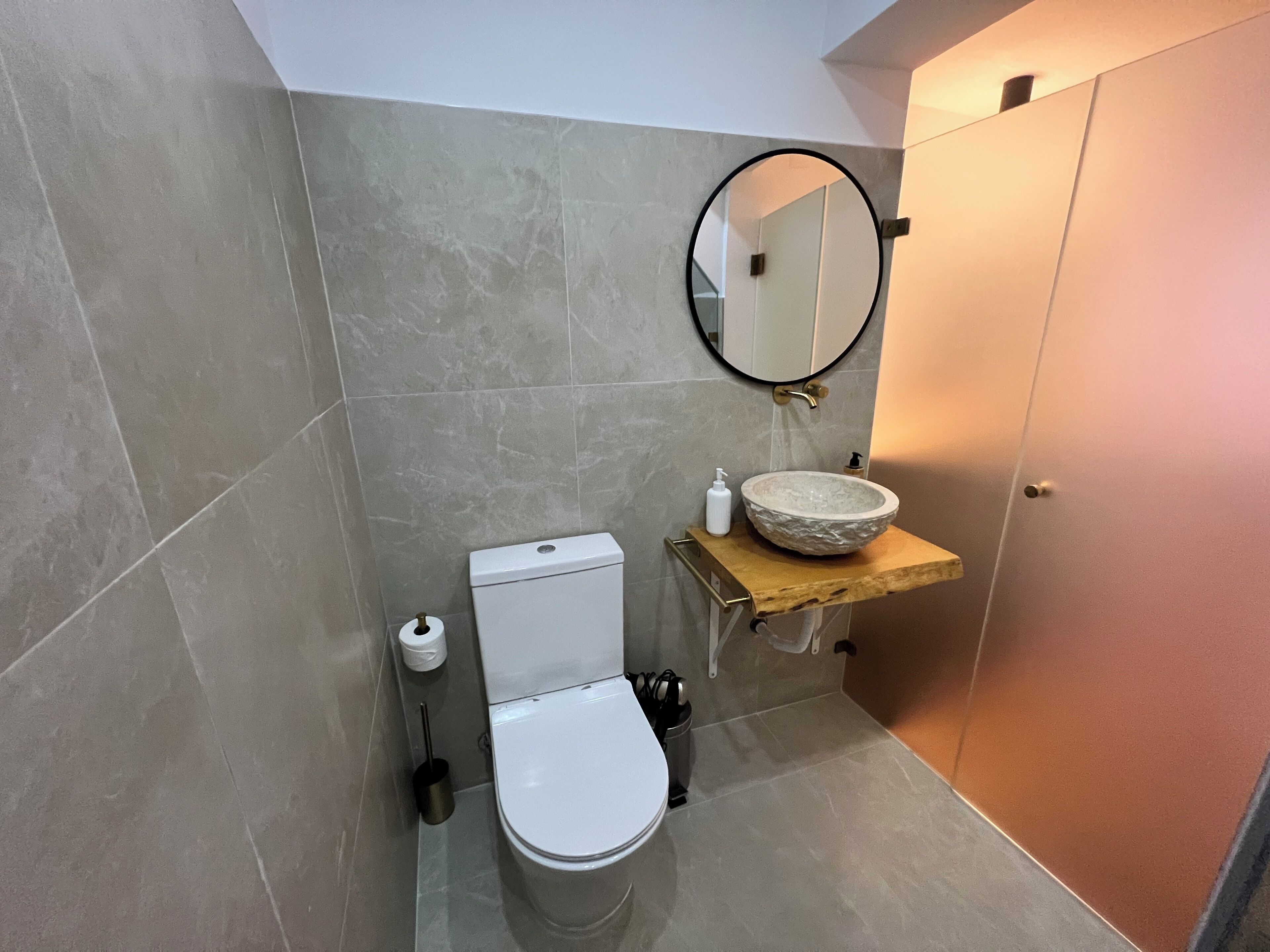 Een badkamer met een toilet, een wastafel met een stenen waskom, een spiegel en een toiletrolhouder.