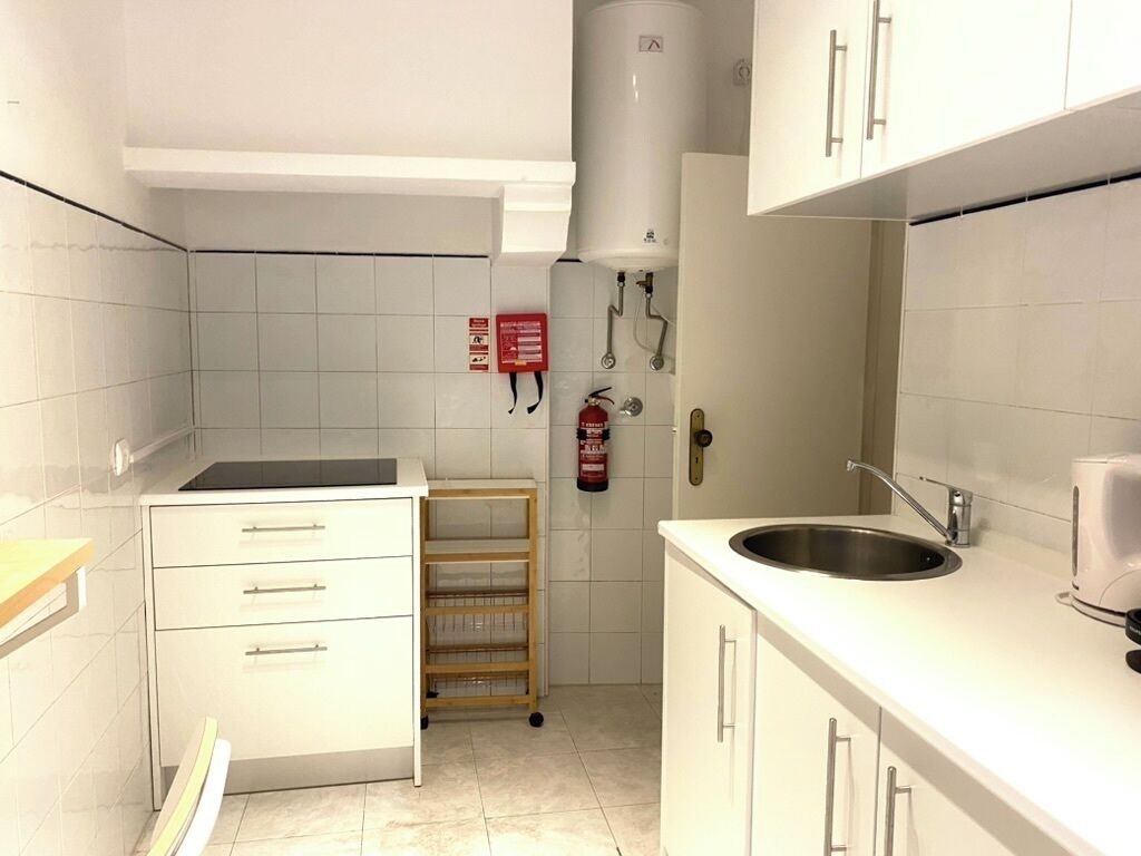 A kitchen with white cabinets, a stainless steel sink, a built-in oven, and a fire extinguisher on the wall.