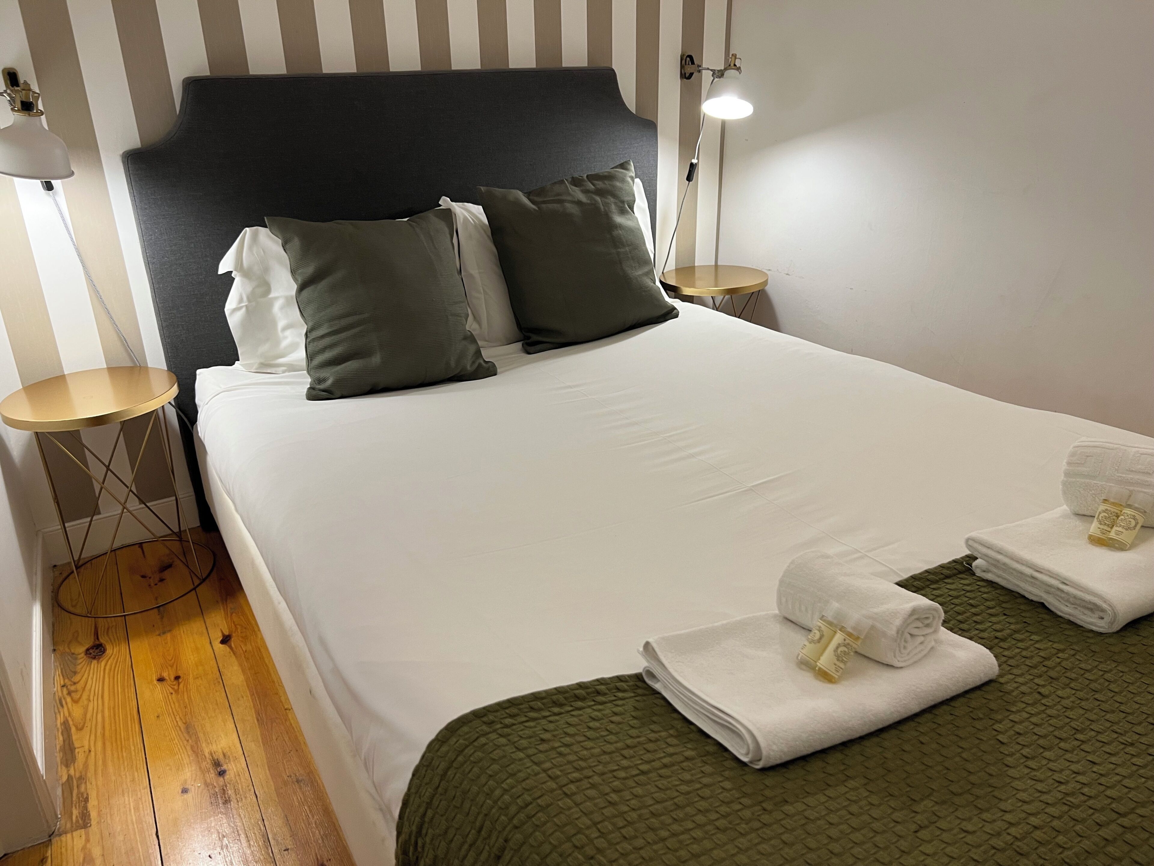 Una cama bien hecha con almohadas, una lámpara de noche y toallas dobladas sobre un edredón verde.