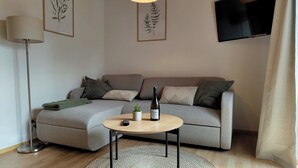 A modern living room with a grey sofa, a round coffee table, a small potted plant, a wine bottle, and framed botanical prints on the wall. - Modern vacation apartment on Lake Constance in Lindau with balcony (Lindau (Bodensee))