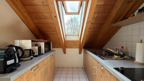 A kitchen with wooden cabinets, a coffee maker, a microwave, a sink, and a skylight. - Modern vacation apartment on Lake Constance in Lindau with balcony (Lindau (Bodensee))