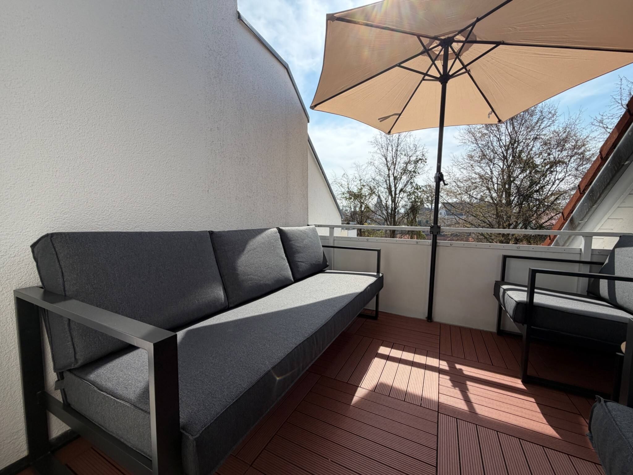 Een balkon met een bank, een stoel en een grote parasol.