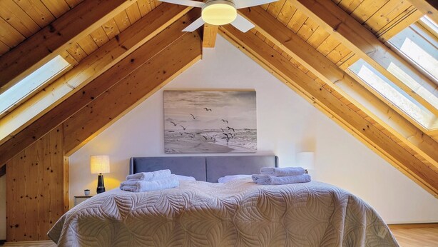 A high-ceilinged room with a large bed, wooden beams, and a skylight. - Modern vacation apartment on Lake Constance in Lindau with balcony (Lindau (Bodensee))