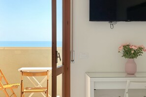 A balcony with a table and chairs, a television mounted on the wall, and a vase with flowers on a table.