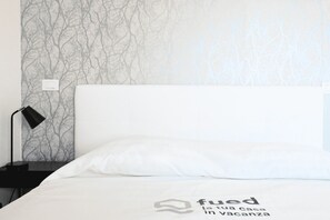 A neatly made bed with a white pillow and a blanket, a black bedside lamp, and a wall with a tree branch pattern.