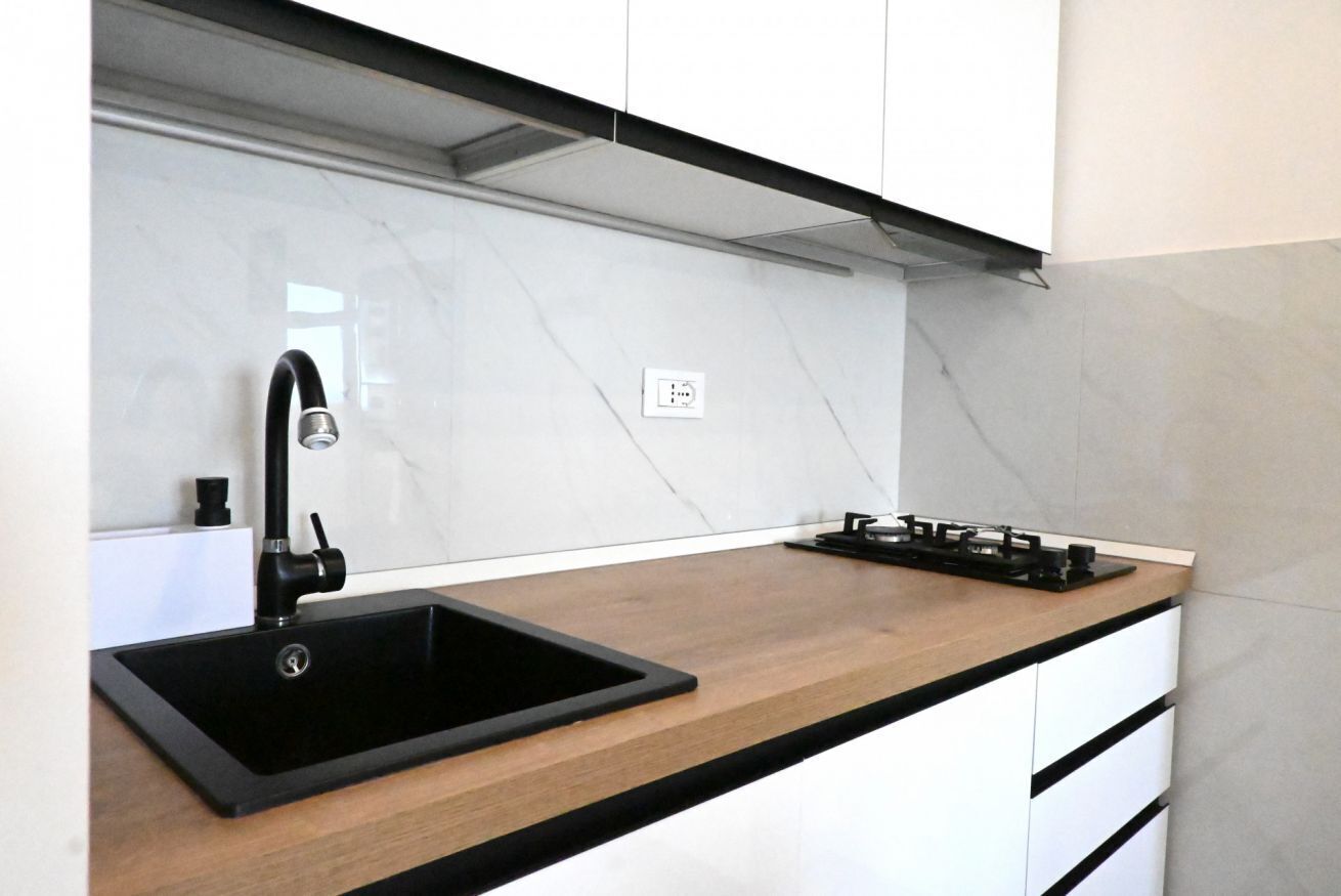 Eine moderne Küche mit einem schwarzen Spülbecken, weißen Schränken und einer Holz Arbeitsplatte.