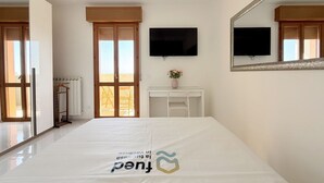 A hotel room with a bed, a television, a mirror, a window with a view, and a radiator. - PSE03 - Porto Sant'Elpidio, sea front charming two-room apartment (San Tommaso Tre Archi, Fermo)