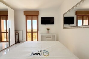 A hotel room with a bed, a television, a mirror, a window with a view, and a radiator.