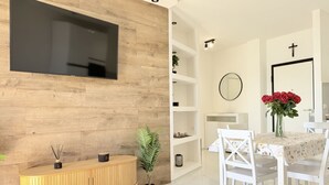 A modern living room with a TV, wooden panel wall, white shelves, a dining table with chairs, and a mirror. - PSE03 - Porto Sant'Elpidio, sea front charming two-room apartment (San Tommaso Tre Archi, Fermo)