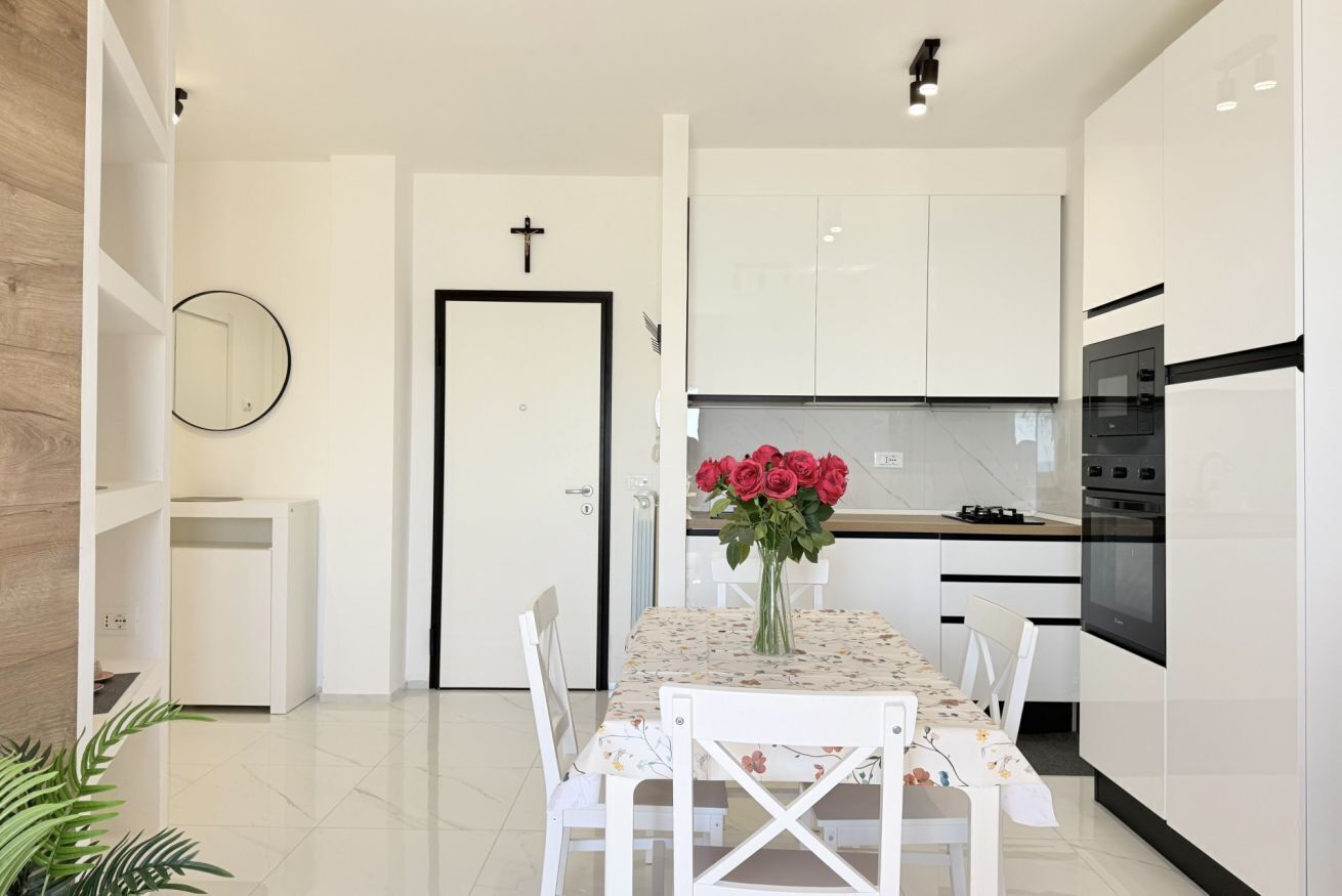 A modern kitchen with white cabinetry, a dining table with chairs, and a vase of red roses.