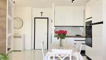 A modern kitchen with white cabinetry, a dining table with chairs, and a vase of red roses.